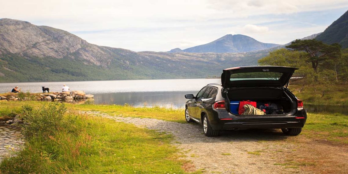 black hatchback with suitcases on a dirt road by a mountain lake