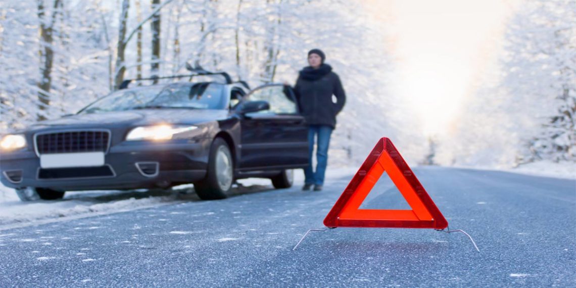 red caution sign on winter road with woman standing beside car stuck in ice