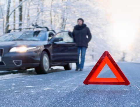 red caution sign on winter road with woman standing beside car stuck in ice