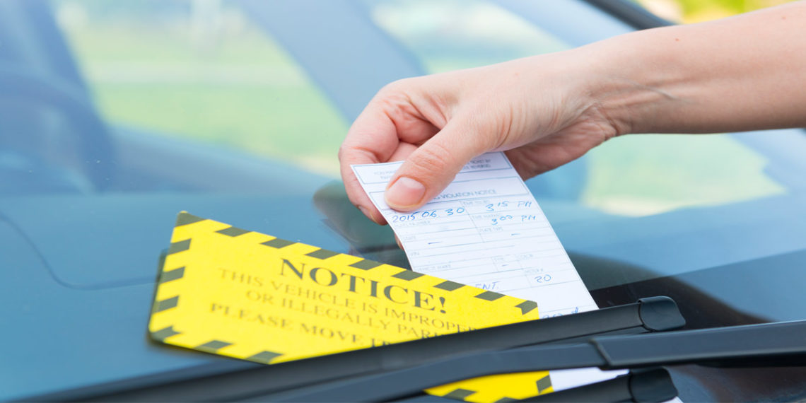 man's hand placing parking ticket under windshield wiper