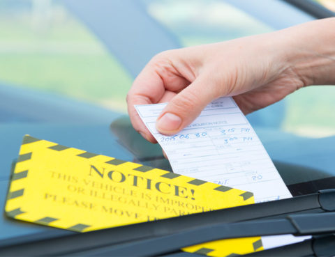 man's hand placing parking ticket under windshield wiper