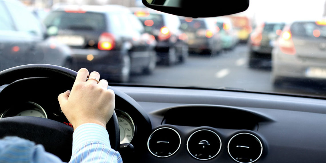 arm of a driver on the steering wheel with bumper to bumper traffic in the background