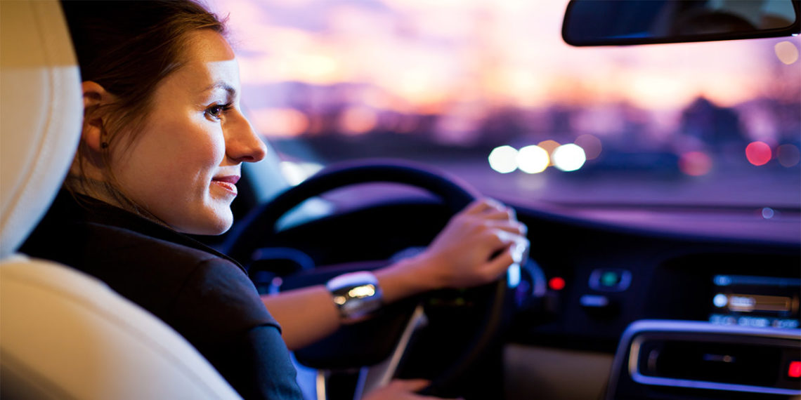 woman driving a car with black and tan interior with blurred landscape in the background