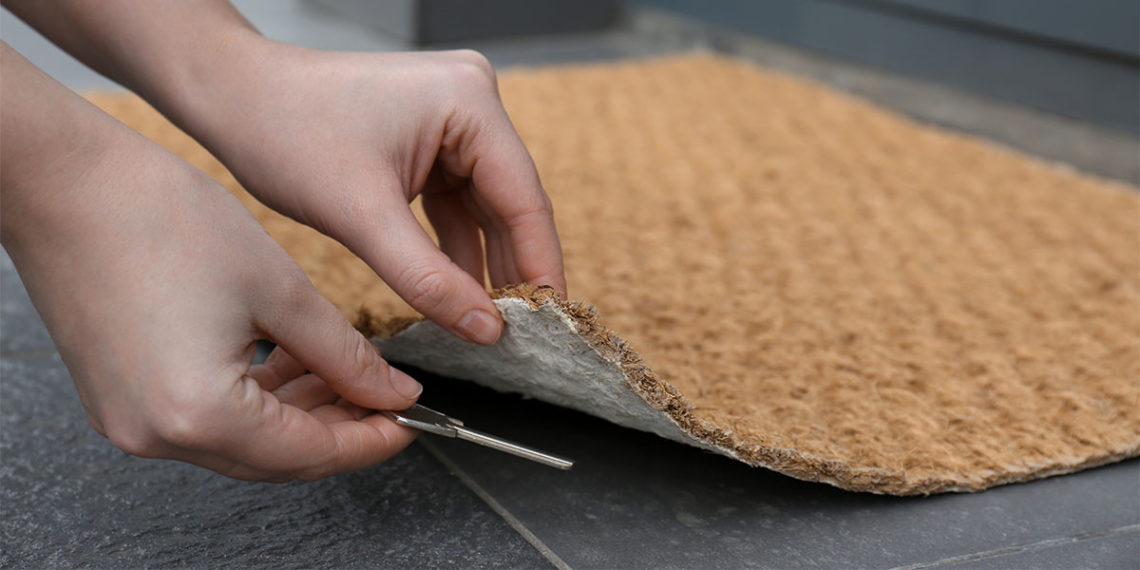 hands lifting up doormat to hide a spare key underneath