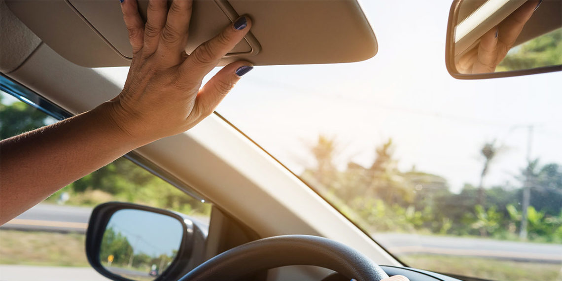 Driver holding up sun visor while driving a car