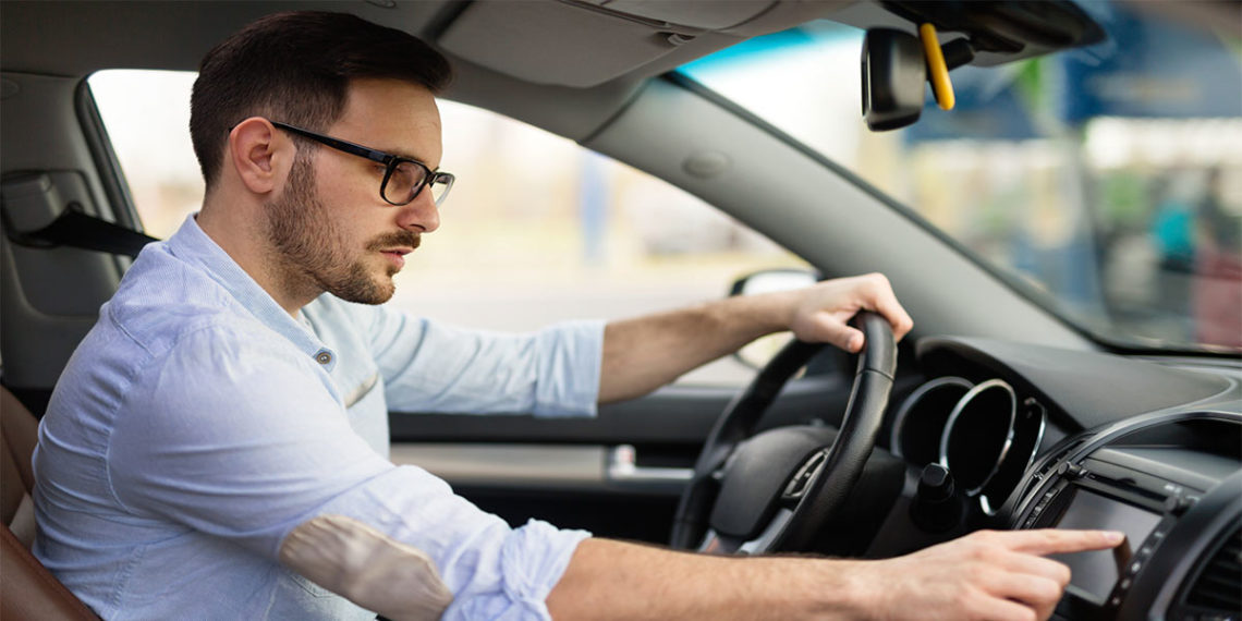 Young man in driver's seat using touchscreen entertainment system on the dash.