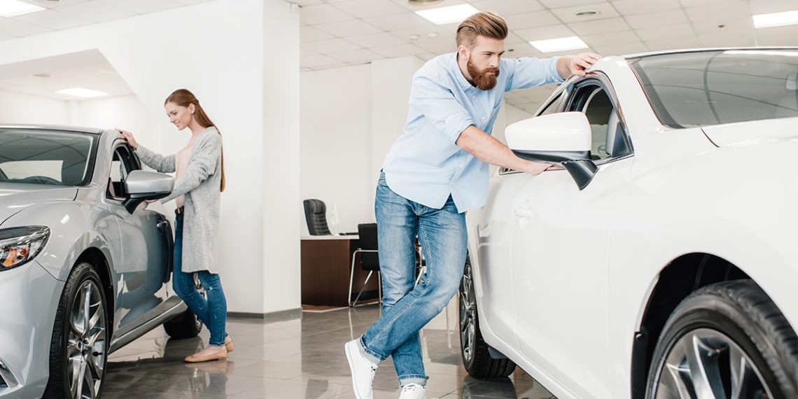 Young man and woman looking at two cars inside a car dealership