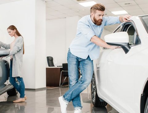 Young man and woman looking at two cars inside a car dealership