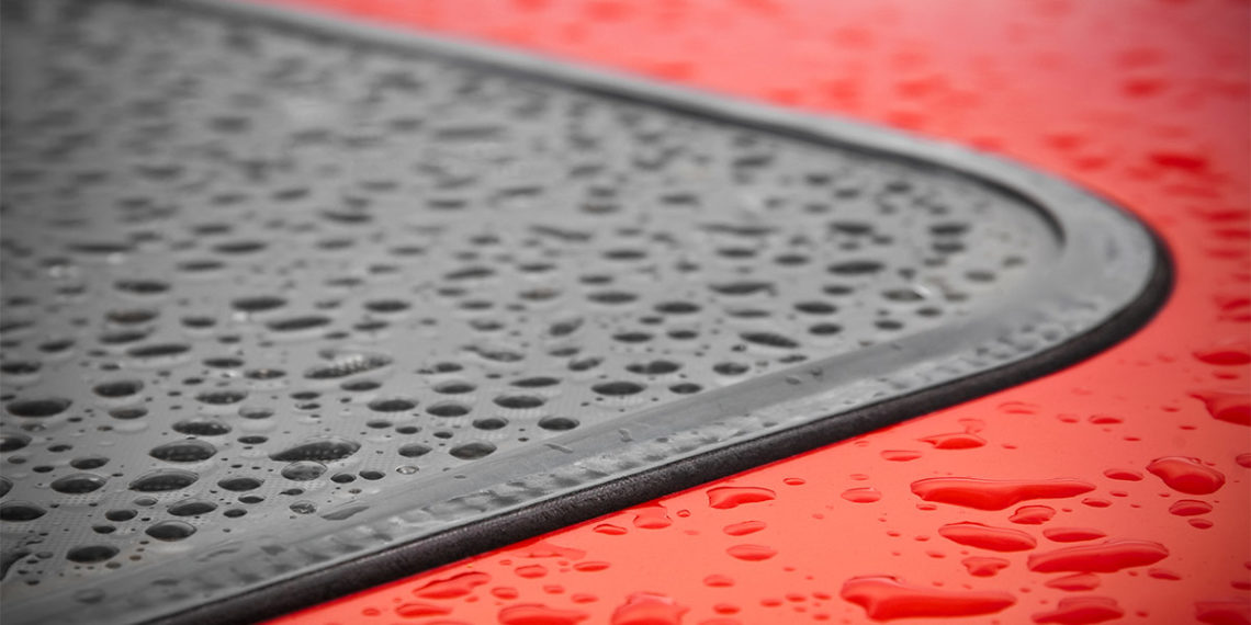 Roof of red car with sunroof covered in water droplets