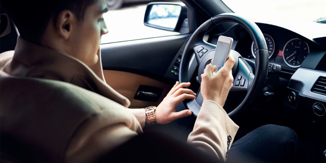 Man in a car texting while sitting in the driver's seat.