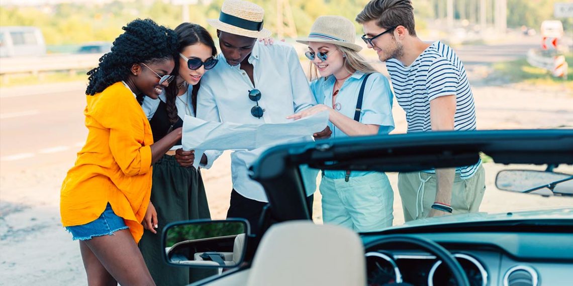 Group of friends standing in front of a car looking at a road map
