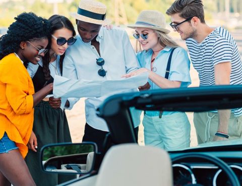 Group of friends standing in front of a car looking at a road map