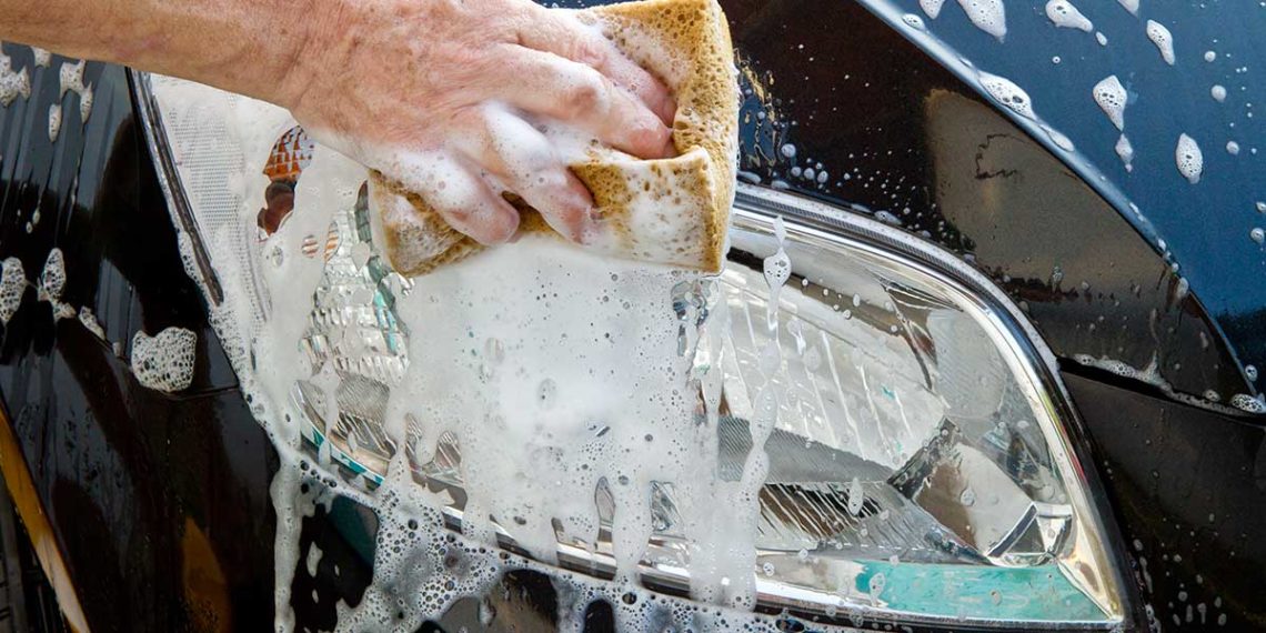 hand squeezing soap from a sponge onto a headlight