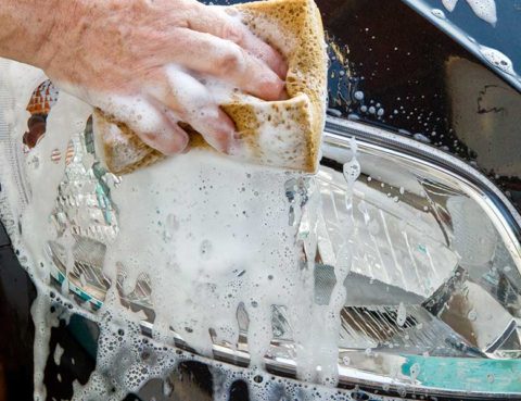 hand squeezing soap from a sponge onto a headlight